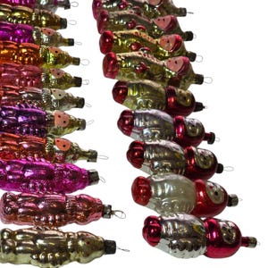 May include: A collection of vintage Christmas ornaments in various colors, including gold, pink, red, and purple. The ornaments are shaped like Santa Claus figures and have small metal loops for hanging. The ornaments are arranged in rows against a white background.