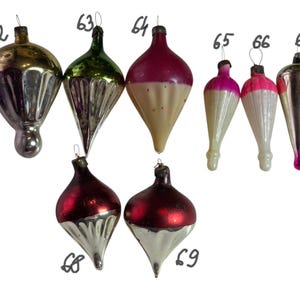 May include: A collection of vintage Christmas ornaments in various shapes and colors. The ornaments include gold, green, red, pink, and silver hues. Some have a bulbous shape, while others are teardrop-shaped. Each ornament has a metal cap and a loop for hanging.