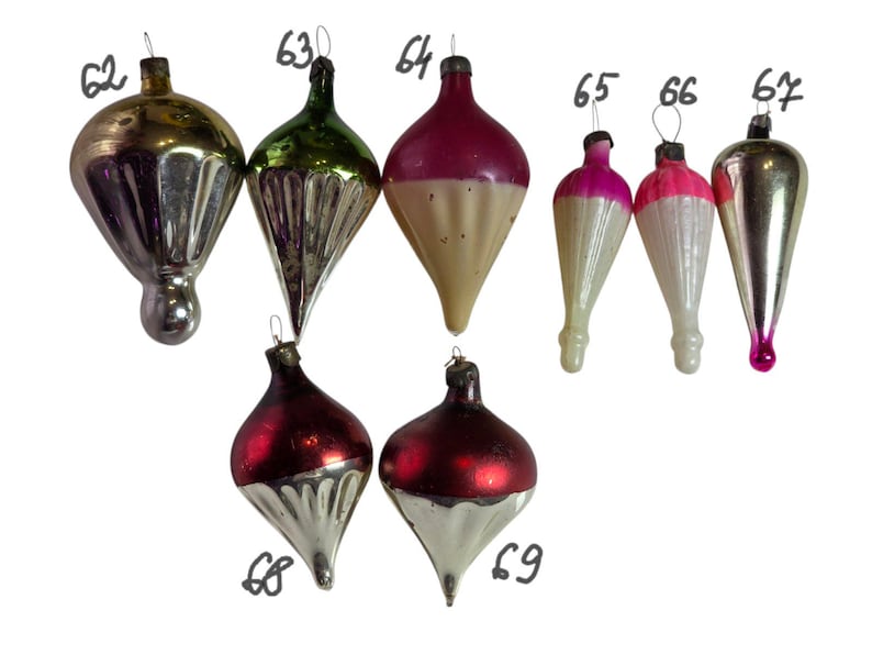 May include: A collection of vintage Christmas ornaments in various shapes and colors. The ornaments include gold, green, red, pink, and silver hues. Some have a bulbous shape, while others are teardrop-shaped. Each ornament has a metal cap and a loop for hanging.