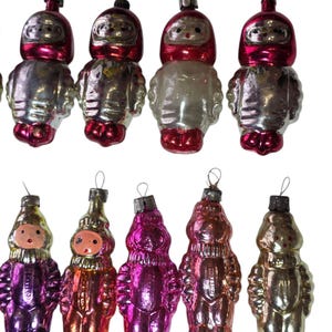 May include: A collection of vintage Christmas ornaments. The ornaments are shaped like figures, with a mix of colors including silver, red, pink, and gold. Each ornament has a loop for hanging.