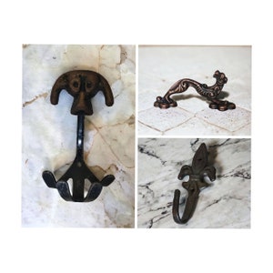 Peut inclure: Trois crochets muraux décoratifs en fonte. Les crochets sont en forme de tête de chien, d'oiseau stylisé et de fleur de lys. Les crochets sont peints dans une finition bronze.