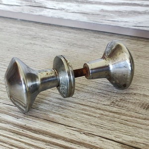 Peut inclure: Deux boutons de porte en argent avec un design en forme de diamant. Les boutons sont reliés par une tige métallique.