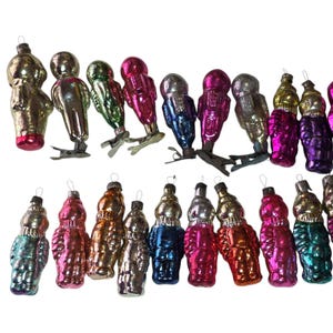 May include: A collection of twenty vintage glass ornaments shaped like figures, featuring a variety of metallic and glossy finishes in colors including pink, gold, blue, green, and silver. Several ornaments include metal clips at the base.