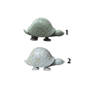Op de afbeelding: Twee plastic speelgoed schildpadden, een groene en een beige, met een nummer 1 en 2 ernaast.
