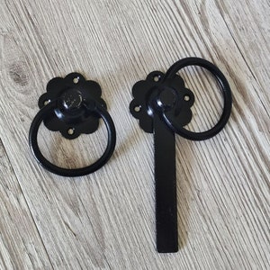 Peut inclure: Loquet de portail en métal noir avec un motif floral décoratif et une poignée en anneau. Le loquet a une barre coulissante qui se verrouille dans la poignée en anneau.
