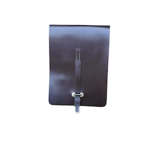 Puede incluir: Una bolsa rectangular de cuero marrón oscuro con un cierre de correa vertical asegurado con una hebilla de metal plateado. La superficie de cuero liso y de color sólido tiene costuras visibles a lo largo de la correa central y esquinas redondeadas.