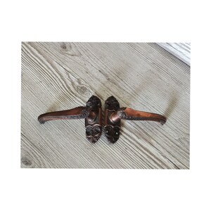 May include: A pair of antique door handles with ornate designs. The handles are made of a dark metal with a copper finish. They are in good condition with no visible damage.