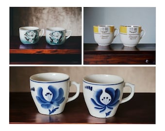 Może przedstawiać: Cztery vintage ceramiczne kubki z kwiatowymi wzorami. Dwa kubki mają wzór kwiatowy w kolorze niebieskim i białym, a dwa kubki mają wzór kwiatowy w kolorze żółtym i złotym z napisem "Französisch April" z przodu.