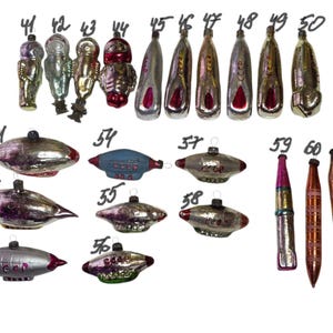 May include: A collection of vintage glass Christmas ornaments shaped like cosmonauts, rockets, and airships, numbered 41 through 61. The ornaments feature metallic finishes in silver, red, and blue, with some displaying the Cyrillic text CCCP.