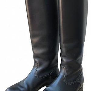 Puede incluir: Un par de botas altas de cuero negro con acabado liso, puntera redondeada y tacón bajo. Las botas presentan una caña alta y estructurada que llega hasta la rodilla, costuras limpias a lo largo del empeine y un diseño sencillo y sobrio.