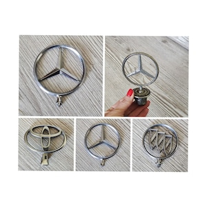 Può includere: Cinque diversi ornamenti per il cofano dell'auto. Gli ornamenti sono tutti argentati e presentano diversi loghi. I loghi includono una stella Mercedes-Benz, un logo Toyota, una stella Mercedes-Benz, un logo BMW e un logo Buick.