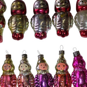 May include: A collection of ten vintage glass ornaments shaped like figures in space suits. The ornaments feature metallic finishes in shades of red, silver, gold, and purple, each topped with a small metal loop for hanging on a tree.