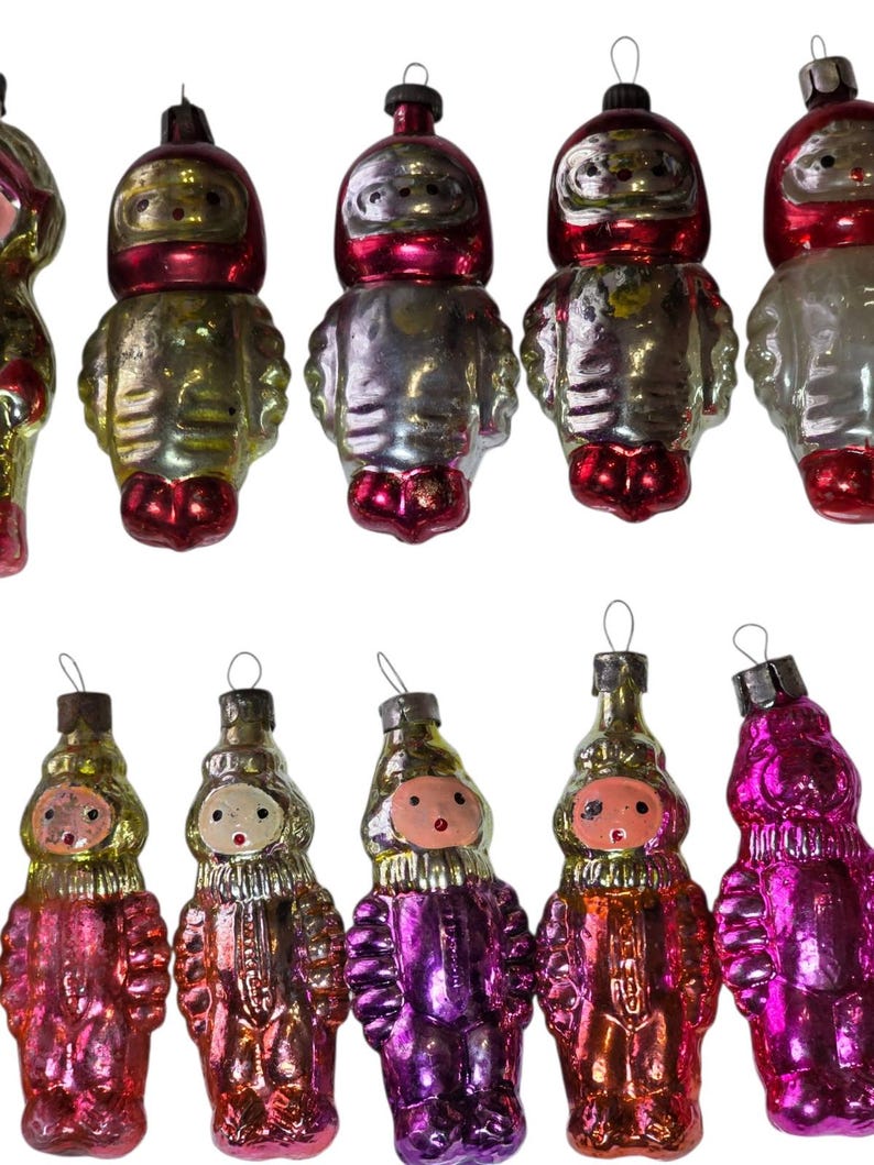 May include: A collection of ten vintage glass ornaments shaped like figures in space suits. The ornaments feature metallic finishes in shades of red, silver, gold, and purple, each topped with a small metal loop for hanging on a tree.