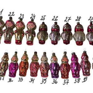May include: A collection of twenty vintage glass ornaments shaped like figures in space suits, numbered 21 through 40. Each ornament features a painted face and metallic finish in various colors including gold, silver, pink, and red.
