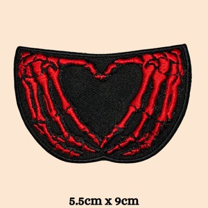 May include: Red embroidered skeleton hands forming a heart shape on a black fabric patch. The patch measures 5.5 inches by 9 inches.