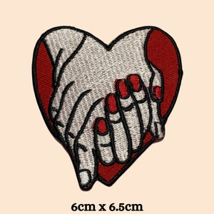 May include: Embroidered iron-on patch of two hands clasped together in the shape of a red heart. The patch measures 6 cm by 6.5 cm.