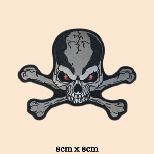 May include: A grey skull and crossbones patch with red eyes. The patch is 8cm by 8cm.