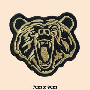Peut inclure: Patch thermocollant brodé noir et or représentant la tête d'un ours avec la gueule ouverte et des dents acérées. Le patch mesure 7 cm sur 8 cm.