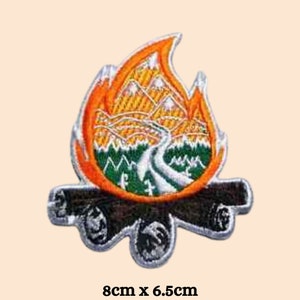 Pode incluir: Um remendo bordado para passar a ferro que apresenta uma fogueira com uma cena de montanha dentro das chamas. O remendo mede 8 cm por 6,5 cm e tem uma combinação de cores preto, laranja, verde e branco.