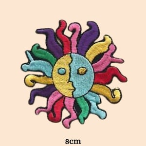 May include: A colourful embroidered patch of a sun with a face. The sun has a yellow and blue face with a purple, pink, red, green, and blue outline. The sun has a yellow eye and a blue eye. The sun has a yellow nose and a blue mouth. The sun has a purple, pink, red, green, and blue outline. The patch is 8 cm in diameter.