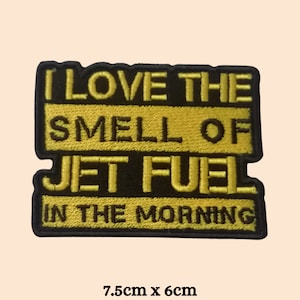 Puede incluir: Parche bordado amarillo con borde negro. El parche dice "Me encanta el olor del combustible de avión por la mañana". El parche mide 7,5 cm por 6 cm.