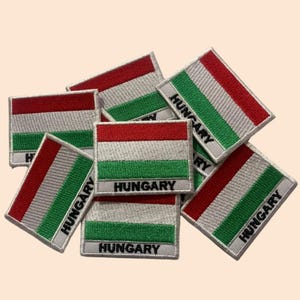 May include: A pile of embroidered iron-on patches featuring the Hungarian flag with the word "HUNGARY" written below. The patches are white with red and green stripes.