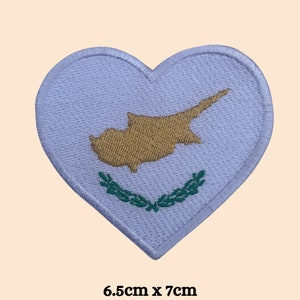 May include: White heart-shaped embroidered patch with the flag of Cyprus. The flag features a gold outline of the island of Cyprus with a green olive branch wreath below. The patch measures 6.5 inches by 7 inches.