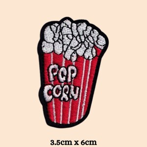Puede incluir: Parche de hierro bordado en rojo y blanco de un cubo de palomitas de maíz con el texto "POP CORN" en blanco. El parche mide 3,5 cm por 6 cm.