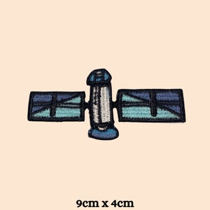 May include: A blue and white embroidered patch of a satellite in space. The patch is 9 cm by 4 cm.