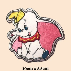 Puede incluir: Parche bordado para planchar con Dumbo el elefante de Disney. El parche es blanco con detalles en rosa y rojo. Dumbo lleva un collar rojo y amarillo y un sombrero rosa. El parche mide 10 cm x 8,5 cm.
