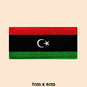 May include: A red, black and green embroidered patch featuring the Libyan flag with a white crescent moon and star. The patch measures 7 cm by 4 cm.