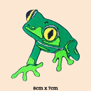 May include: Green embroidered frog patch with a yellow eye. The patch is 8 cm by 7 cm.