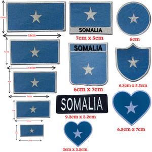 Op de afbeelding: Een verzameling geborduurde patches met de blauwe vlag met witte ster van Somalië in verschillende vormen en maten, waaronder rechthoeken, cirkels, schilden en harten, waarbij sommige patches zijn voorzien van de tekst SOMALIA in het wit.