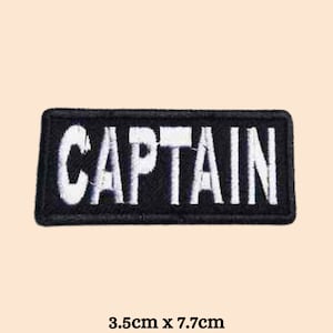 Könnte beinhalten: Schwarzer gestickter Aufnäher mit weißer Beschriftung "CAPTAIN". Der Aufnäher ist 3,5 cm x 7,7 cm groß.