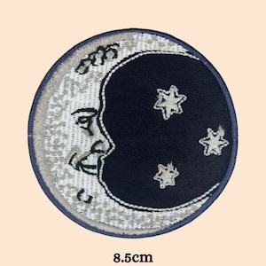 May include: A white and gray embroidered crescent moon with a face and three white stars on a black background. The patch is 8.5 cm in diameter.