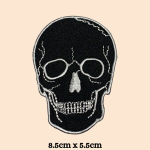 May include: Black embroidered skull patch with white stitching. The skull has a detailed design with eye sockets, a nose, and a mouth. The patch measures 8.5 inches by 5.5 inches.