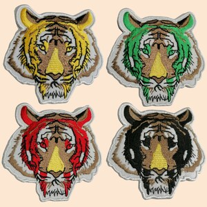 Puede incluir: Cuatro parches bordados para planchar con caras de tigre en diferentes colores: amarillo, verde, rojo y negro. Cada parche tiene un contorno blanco y una nariz marrón.