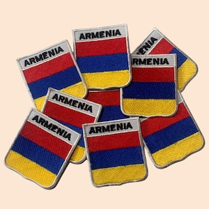 May include: A pile of ten embroidered iron-on patches featuring the Armenian flag. Each patch is rectangular with a white background and the word "Armenia" printed in black at the top. The flag is red, blue, and orange.