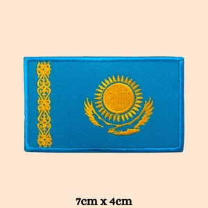 May include: A blue embroidered patch featuring the flag of Kazakhstan. The flag depicts a golden sun with rays and a stylised eagle on a blue background. The patch measures 7cm by 4cm.
