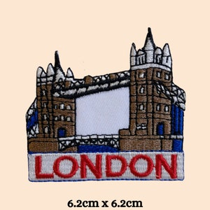 May include: Embroidered patch featuring a brown and white illustration of Tower Bridge in London, with a blue and white bridge and the word "LONDON" in red letters on a white and blue banner. The patch measures 6.2 cm by 6.2 cm.