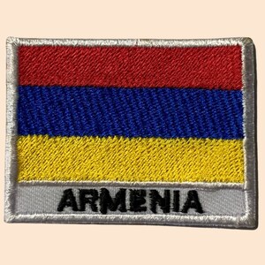 May include: An embroidered patch featuring the flag of Armenia. The patch is rectangular and has a white border. The flag is red, blue, and orange with the word "ARMENIA" written in black below the flag.