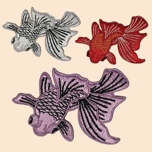 Op de afbeelding: Drie geborduurde strijkbare patches van goudvissen. Eén is zilver, één is rood en één is paars.