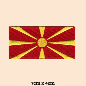 May include: Embroidered patch of the flag of North Macedonia. The flag is red with a yellow sun in the center and eight yellow rays extending from the sun.