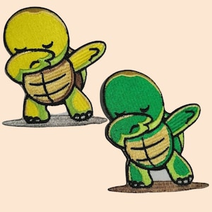 May include: Two embroidered iron-on patches of cartoon turtles doing the 'dab' pose. One turtle is green and the other is yellow.