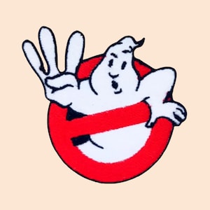 May include: A red and white embroidered patch featuring the Ghostbusters logo. A white ghost with a mischievous expression is holding up three fingers, surrounded by a red circle with a diagonal line through it.