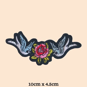 May include: Black embroidered patch featuring two blue and white birds facing each other with a pink and red rose in the centre. The patch measures 10cm x 4.5cm.