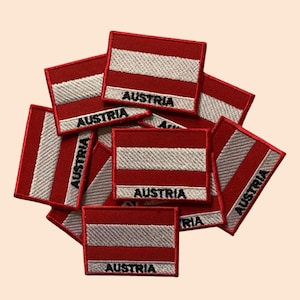 May include: A pile of red and white embroidered iron-on patches with the word "Austria" written on each patch.
