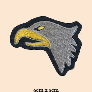 May include: A gray embroidered eagle head patch with a yellow beak and eye. The patch is 6 cm by 5 cm.
