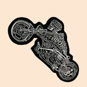 Pode incluir: Um remendo bordado em preto e branco de um esqueleto a andar de moto. A moto está na roda traseira e o esqueleto está a usar um capacete.