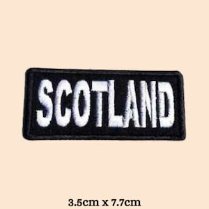 May include: Black embroidered patch with white lettering that reads "SCOTLAND". The patch is 3.5 cm by 7.7 cm.